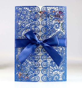Detail of laser-cut royal blue lace wedding invitation with glitter finish and satin bow