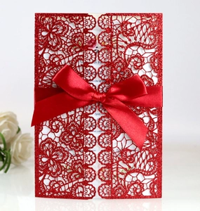 Detail of red glitter laser-cut invitation card with floral patterns and a satin ribbon bow