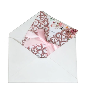 Detail of laser-cut rose gold glitter wedding invitation with pink bow and floral insert