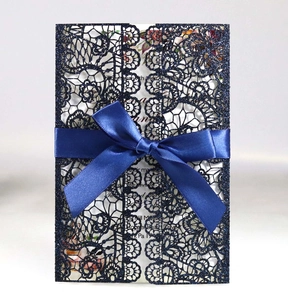 Detail of navy blue glitter laser-cut lace invitation with a silk ribbon bow