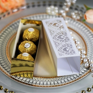 White laser-cut heart pattern gift box with three gold chocolates on a floral plate