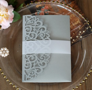 Silver laser cut wedding invitation with intricate vine pattern on elegant glass tray