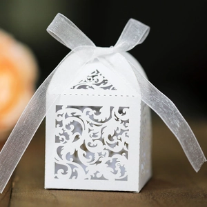 White laser cut lace wedding favor box with ribbon on wooden surface for party candy