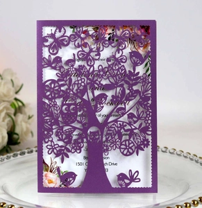 Close-up of laser-cut purple invitation card featuring birds, butterflies and a tree