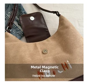 Close-up of metal magnetic buckle on the dark khaki suede bag with MOCHI embroidery