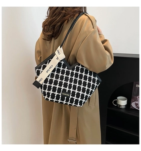 Detail view of the black and white plaid woven tote bag featuring a leather edge and logo plate