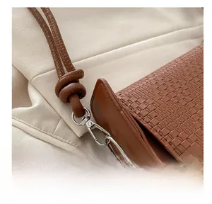Detail of silver metal hook and woven brown leather texture on a crossbody handbag