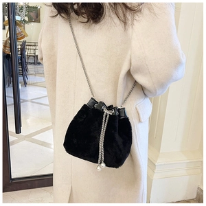 Détail du sac seau en fausse fourrure noire avec cordon perlé sur un mannequin en manteau