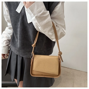 Detail of khaki shoulder bag featuring an asymmetric flap and unique knotted strap design