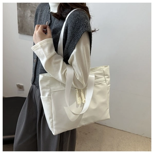 Detail of white nylon tote bag with wide strap handles and braided rope zipper pulls