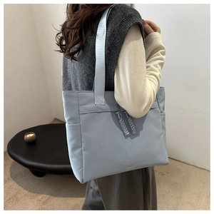 Light blue tote bag with woven zipper detail and side pocket shown on a model