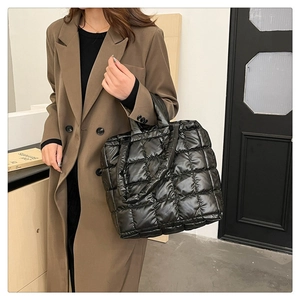 Detail of a large black quilted tote bag with smooth finish and wide shoulder handles