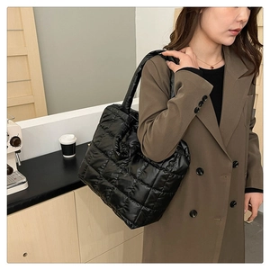 Detail shot of the black quilted puffer tote bag worn over the shoulder by a model