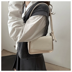 Detail of a beige shoulder bag featuring woven texture and unique knotted strap design