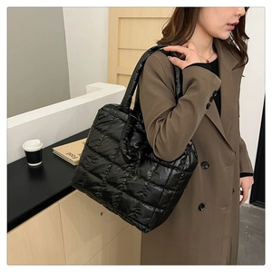 Close-up of black quilted puffer tote bag with wide shoulder strap on wool coat