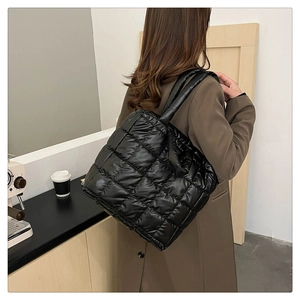 Detail view of black quilted puffer tote bag in nylon material carried by a model