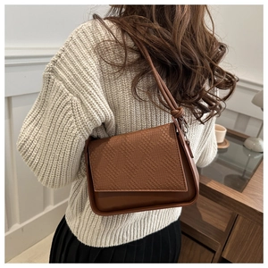 Close-up of brown crossbody baguette bag featuring woven texture flap and smooth finish