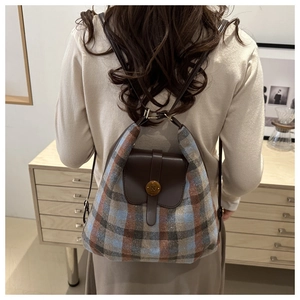 Détail du sac à dos à carreaux montrant le tissu texturé et le rabat en cuir brun sur modèle
