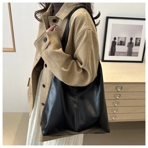 Detail of a black large tote bag in matte PU leather shown in a lifestyle indoor setting