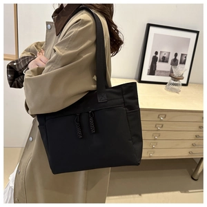 Black nylon tote bag detail with side pocket and zipper pockets in a lifestyle setting