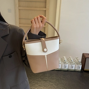 Detail of color-block bucket bag in light coffee and white leather held by model