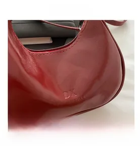 Detail of dark red faux leather crescent bag featuring embossed brand lettering logo