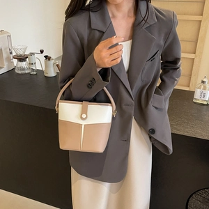Detail of a minimalist two-tone bucket bag in cream and mocha brown with elegant handle