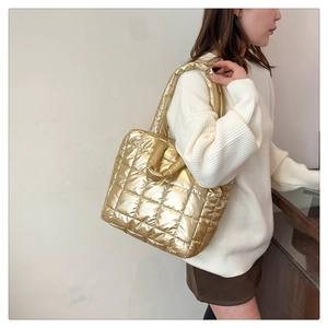 Close-up of golden quilted puffer tote bag being worn as a shoulder bag on model