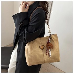 Détail du sac cabas camel avec plaque logo triangle et breloque ours en peluche marron