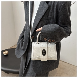 Détail d'un sac à main blanc motif crocodile avec fermoir noir sur une veste en laine grise