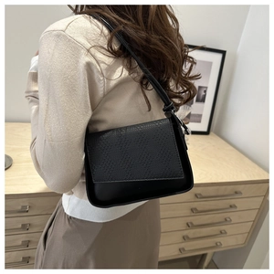 Detail view of black shoulder bag with woven flap and smooth leather texture on model