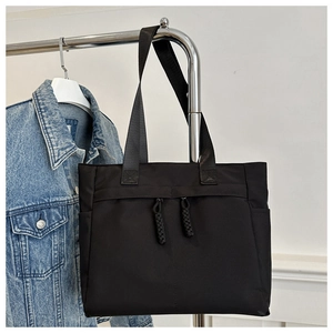 Detail of black nylon tote bag with front zipper pockets and braided cord pullers