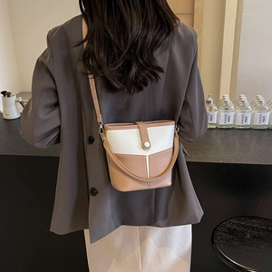 Rear view of model wearing a two-tone white and khaki bucket bag with adjustable strap