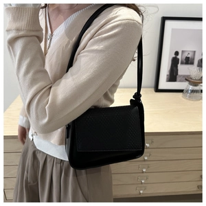 Close-up of the textured woven flap and minimalist strap of this black leather crossbody bag