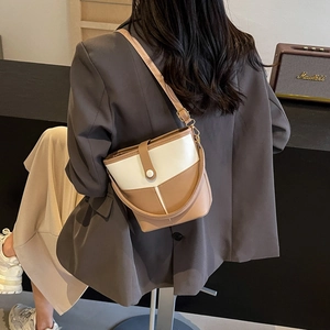Detail view of khaki and cream bucket bag worn as a shoulder bag on a grey blazer