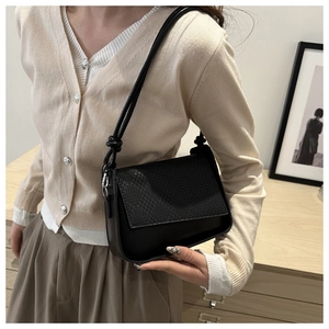 Detailed close-up of black leather handbag featuring woven flap texture and dual slim straps