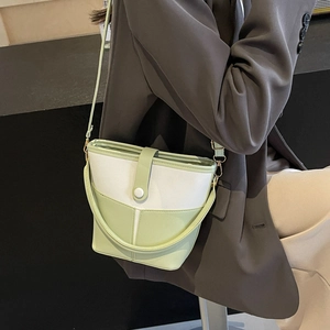 Green and white patchwork bucket bag with crossbody strap shown on a gray suit