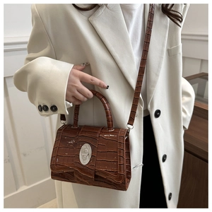 Sac à main marron à motif crocodile et fermoir argenté sur une veste de blazer blanche