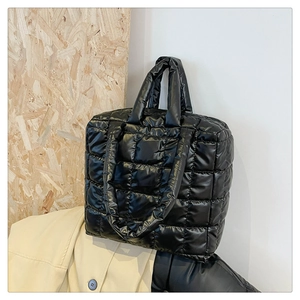 Detail of black quilted puffer tote bag showing glossy nylon fabric and large square stitching