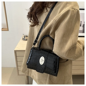 Détail du sac noir à motif crocodile avec fermoir rotatif argenté sur manteau