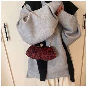 Détail du sac léopard rouge avec bordure dorée et fermoir perle porté par un mannequin