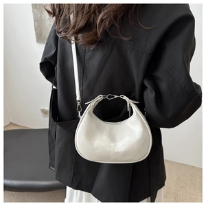 Detail shot of a white crescent moon handbag with shiny finish on a model shoulder