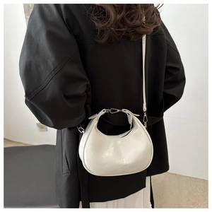 Close-up of a white crescent shoulder bag with glossy PU leather and silver hardware