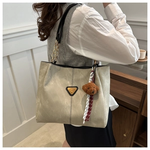 Détail du sac cabas kaki avec plaque triangulaire en métal et porte-clés en forme d'ourson