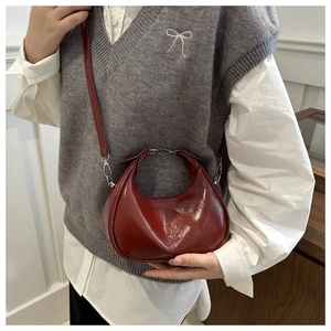 Detail of dark red patent leather crescent bag with glossy finish and brand lettering