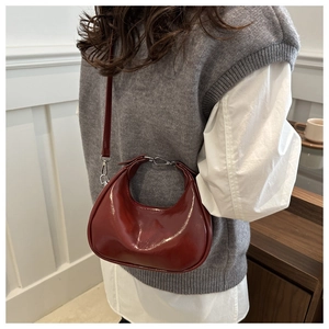Detailed view of deep red patent leather crescent bag on a model showing shiny texture