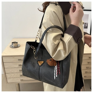 Vue détaillée du grand sac cabas noir en cuir avec logo triangulaire doré et breloque ours