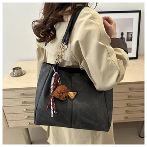 Détail du sac cabas noir avec logo triangle doré, charm ours en peluche et bandoulière