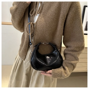 Close-up of a glossy black patent leather crescent bag with DX embossed detail