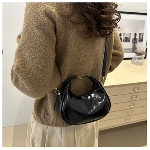 Glossy black hobo bag with silver hardware worn over the shoulder in a cozy interior